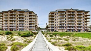 A beachfront hotel with multiple balconies, a wooden walkway leading to the entrance, and a sandy beach area. - 59-ocean-place (Fernandina Beach)
