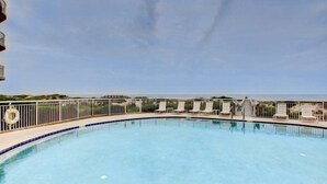 A swimming pool with a view of the ocean, surrounded by a fence and lounge chairs. - 59-ocean-place (Fernandina Beach)