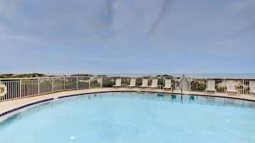 Piscina com vista para o oceano, cercada por uma grade e cadeiras de sol.
