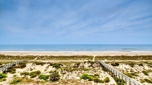 A coastal landscape with a sandy beach, grassy dunes, and a wooden boardwalk leading to the sea. - 59-ocean-place (Fernandina Beach)