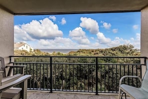 A balcony with a view of the beach and ocean, featuring a black metal railing and two chairs.