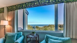 A room with two light blue sofas, a small table with a plant, and a view of the ocean through large windows.