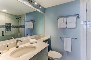 A bathroom with a large mirror, a sink, a toilet, and a shower.