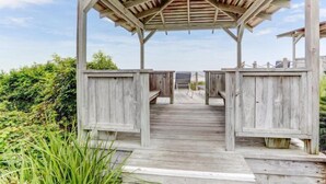 A wooden deck leading to a covered pavilion with a view of the surrounding greenery.