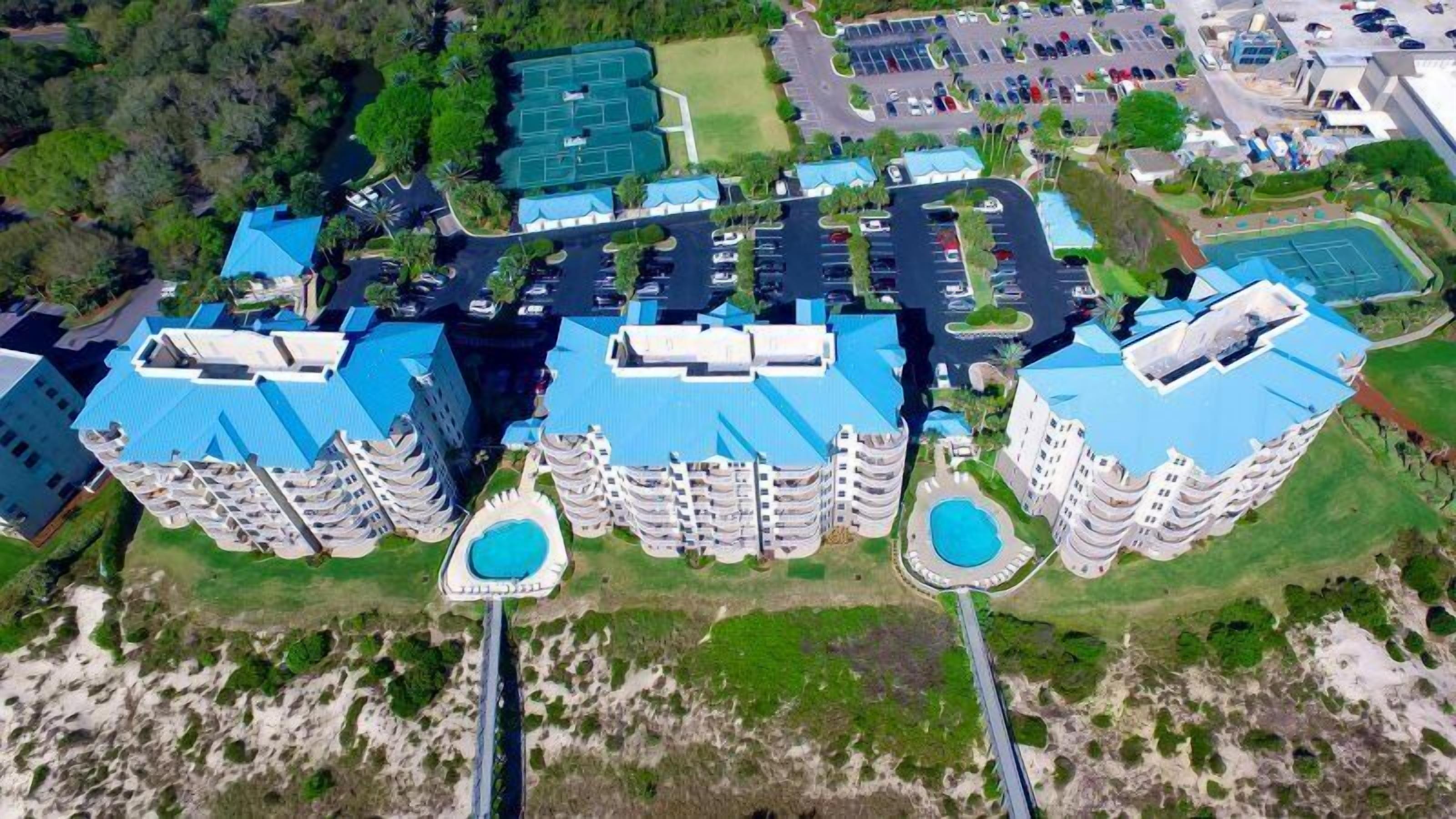 A high-rise hotel with multiple blue-roofed buildings, a central pool, and a parking lot.