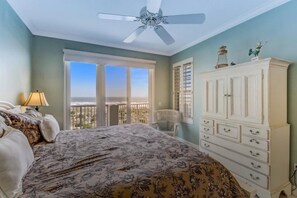 A bedroom with a bed, a dresser, a chair, and a view of the ocean through a window. - 13-ocean-place (Fernandina Beach)