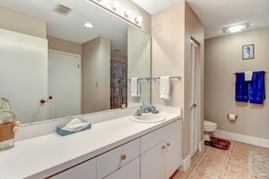 A bathroom with a white vanity, a large mirror, a sink, and a toilet.