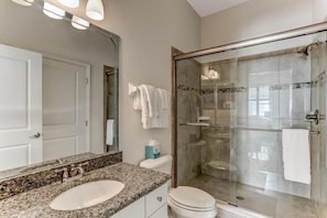 A bathroom with a granite countertop sink, a glass shower enclosure, and a white toilet.