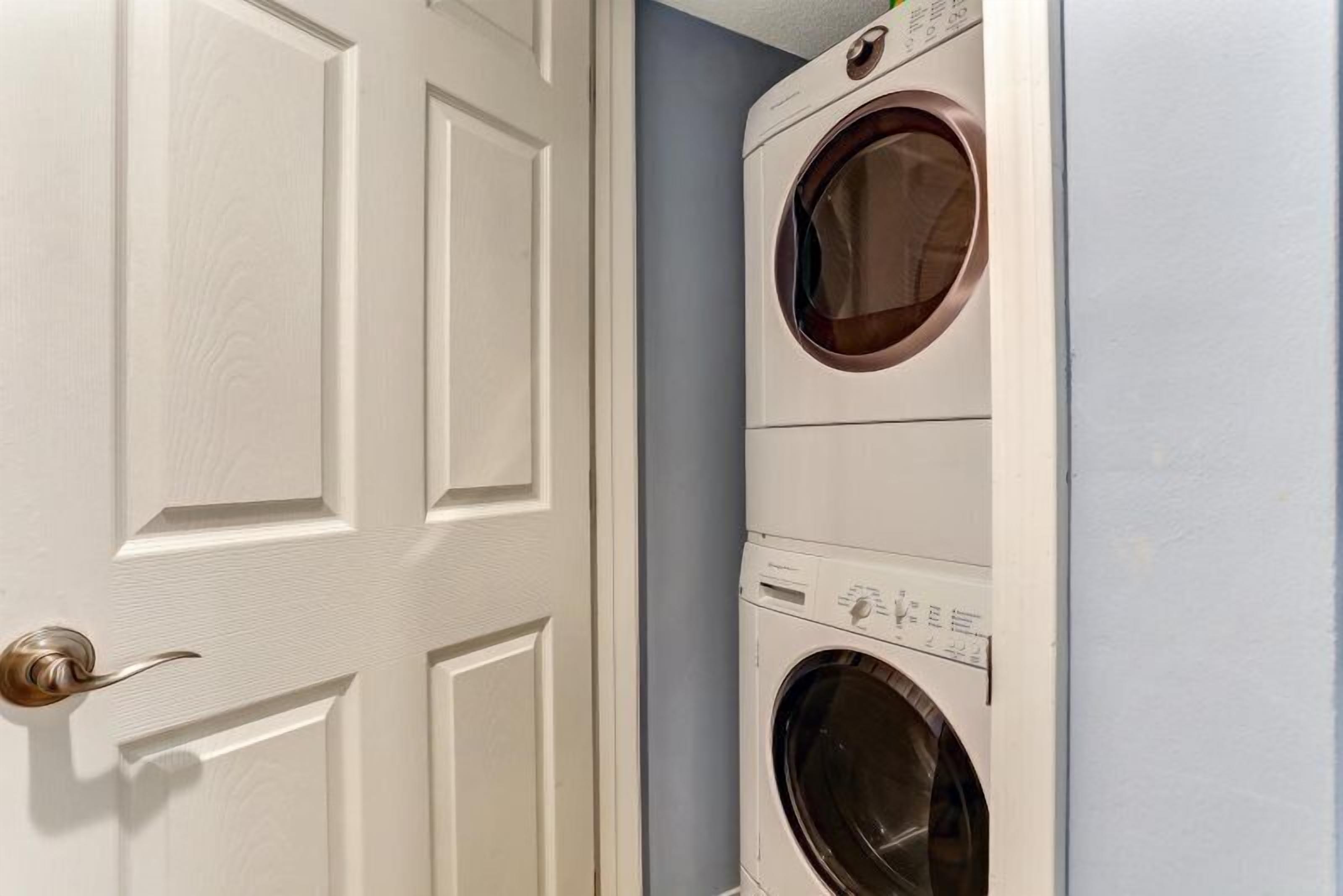 A laundry room with two stacked front-loading washing machines and a white door with a brass handle.