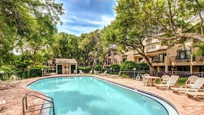 Une piscine avec des chaises longues et un petit bâtiment, le tout entouré d’arbres et d’une clôture.