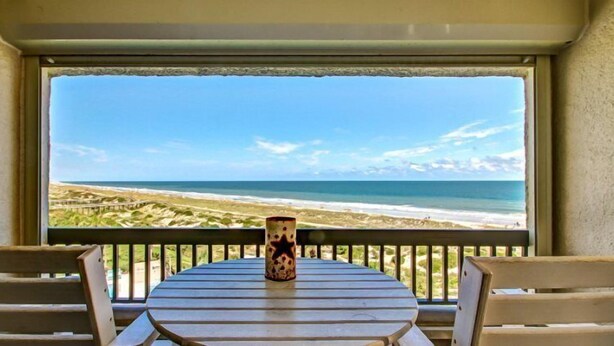 Een tafel met een vaas met sterrenpatroon, met uitzicht op een strand met golven en een heldere lucht.