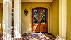 A wooden double door with glass panels, a tiled entrance area, and a wall-mounted lantern. - 14-sweetwater-oaks-drive (Fernandina Beach)