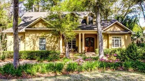 A two-story house with a front porch, a chimney, and a well-maintained garden with various plants and flowers. - 14-sweetwater-oaks-drive (Fernandina Beach)