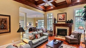 A spacious living room with a fireplace, a sofa, a coffee table, and a dining area in the background. - 14-sweetwater-oaks-drive (Fernandina Beach)