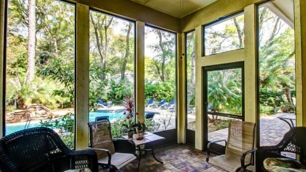 A sunroom with large windows overlooking a pool and lush greenery. - 14-sweetwater-oaks-drive (Fernandina Beach)