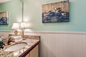 A bathroom with a marble sink, two wall-mounted lamps, and two bird-themed paintings. - 608-sailmaker (Fernandina Beach)