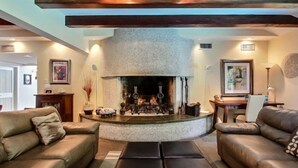 A cozy living room with a stone fireplace, leather sofas, and a wooden ceiling beam. - 17-beach-walker-road (Fernandina Beach)