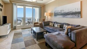 A living room with a sofa, coffee table, and a ceiling fan. There is a sliding glass door leading to an outdoor area with a table and chairs. - 88-ocean-place (Fernandina Beach)