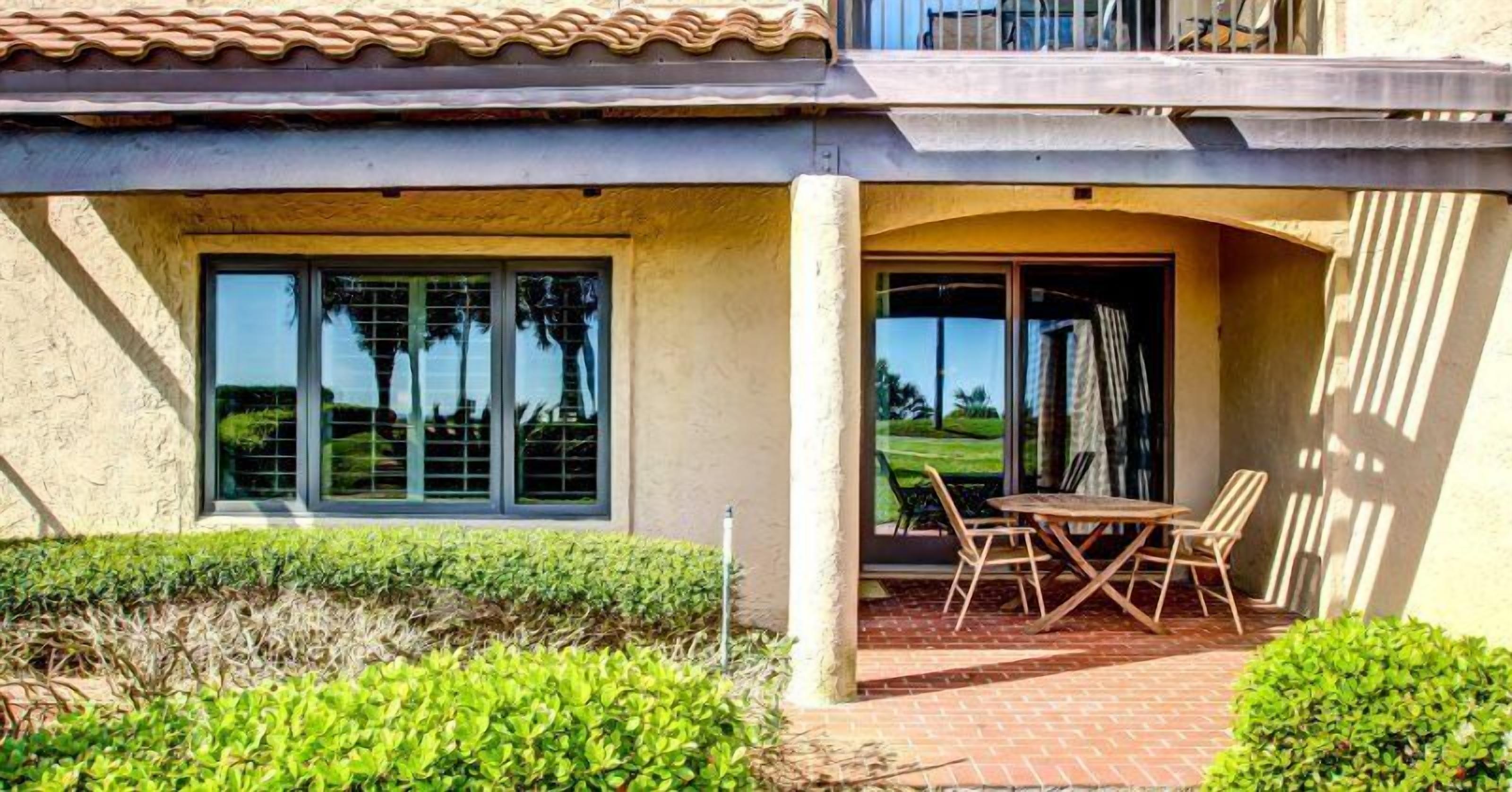A house with a patio area featuring a table and chairs, large windows, and a view of a golf course.
