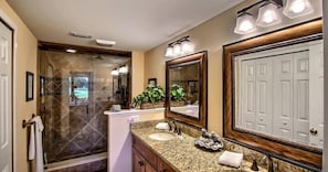 A bathroom with a glass shower enclosure, a sink with a granite countertop, and a large mirror above the sink.