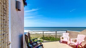 A balcony with a view of the ocean, featuring two white chairs and a striped chair. - 1196-beach-walker (Fernandina Beach)