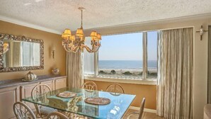 A dining area with a glass table, chairs, a chandelier, a view of the beach, and a large mirror. - 1135-beach-walker (Fernandina Beach)
