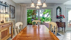 A dining area with a wooden table and chairs, a chandelier, and a view of greenery outside. - 3062-club-villas (Fernandina Beach)