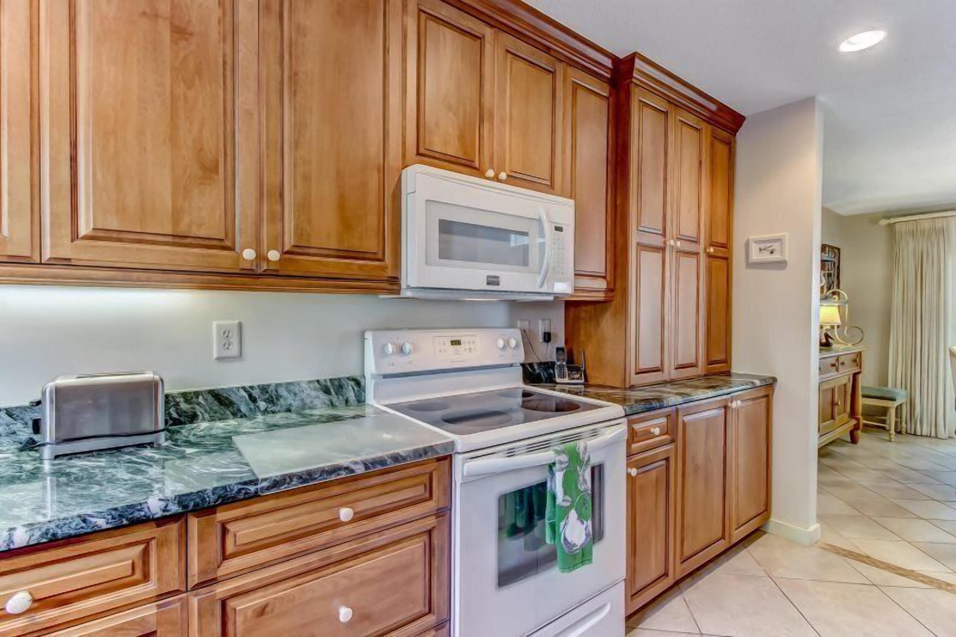 A kitchen with wooden cabinets, a white microwave, a stove, and a marble countertop.