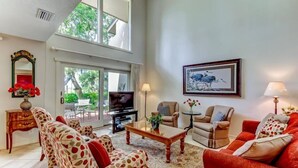 A spacious living room with a large window, a television, and a framed artwork on the wall. - 3062-club-villas (Fernandina Beach)