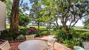 A patio with a round table and chairs, surrounded by lush greenery and trees with Spanish moss. - 3062-club-villas (Fernandina Beach)