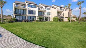 Un edificio moderno de varios pisos con balcones, un césped cuidado y palmeras.