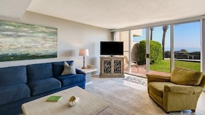 Una sala de estar moderna con un sofá azul, un sillón verde, una mesita de centro y un televisor sobre un mueble.