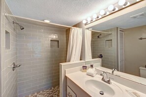Une salle de bain avec une douche, un lavabo, un miroir et des luminaires au-dessus du miroir.