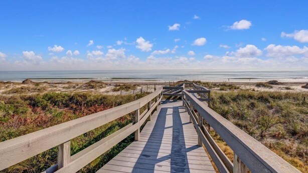 Un paseo marítimo de madera que conduce a una playa con dunas y vegetación escasa.