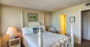 A bedroom with a four-poster bed, a bedside table with a lamp, and a door leading to another room.