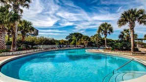 Una piscina con bordo curvo, circondata da palme e un cielo azzurro limpido.