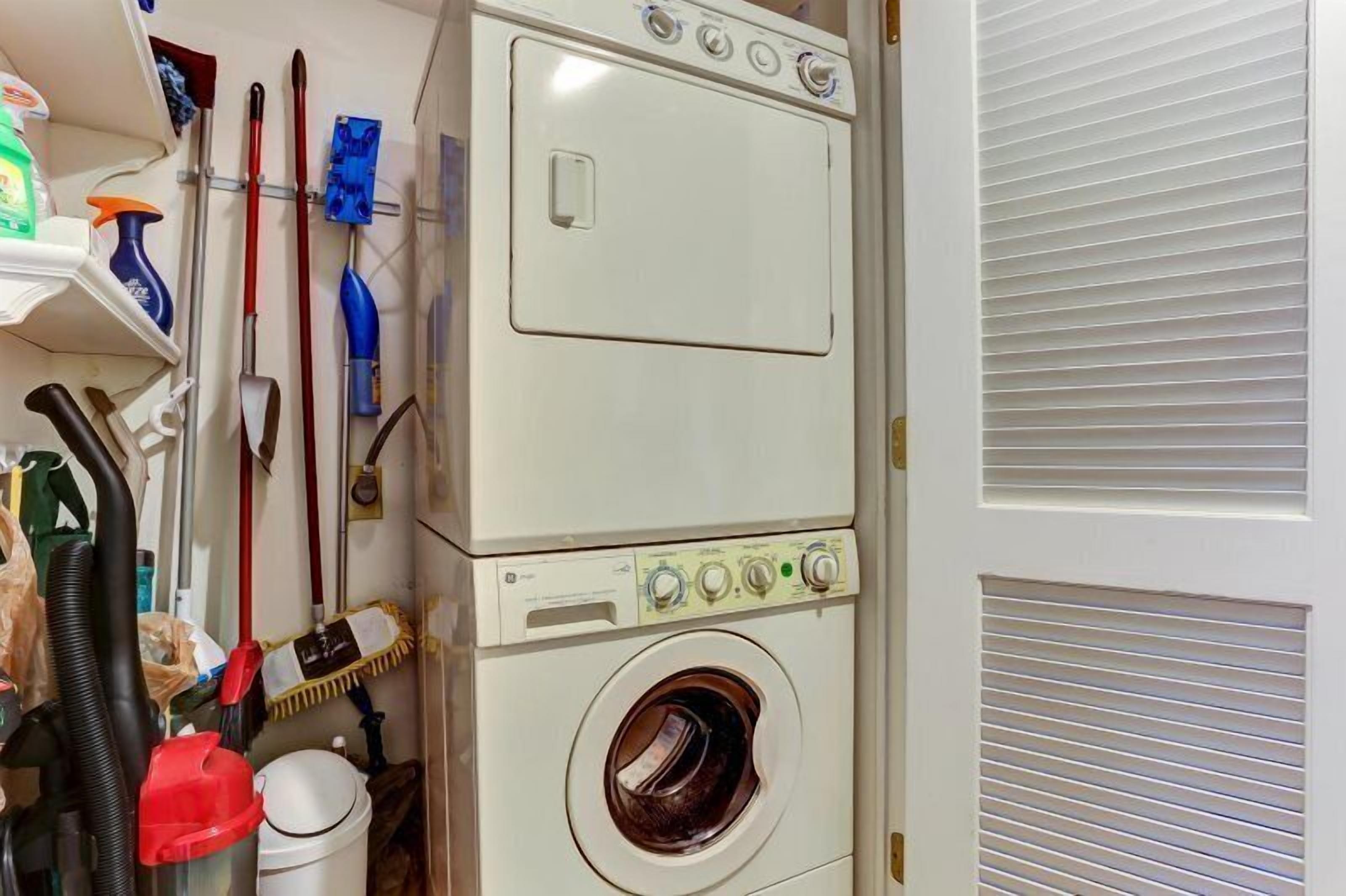 A laundry room with stacked washers and dryers, a mop, brooms, and cleaning supplies.