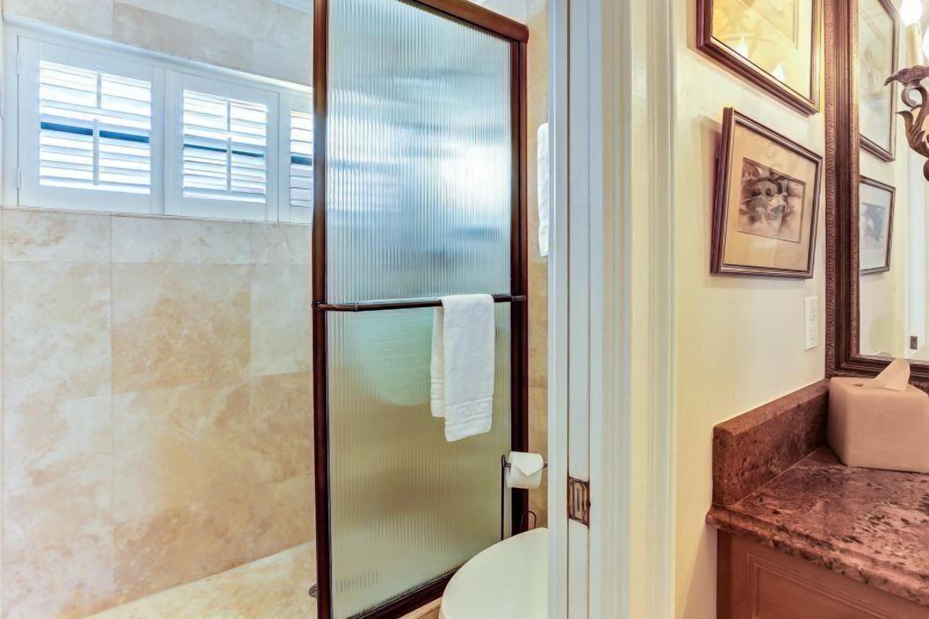 A bathroom with a glass shower enclosure, a marble countertop, and framed artwork on the wall.