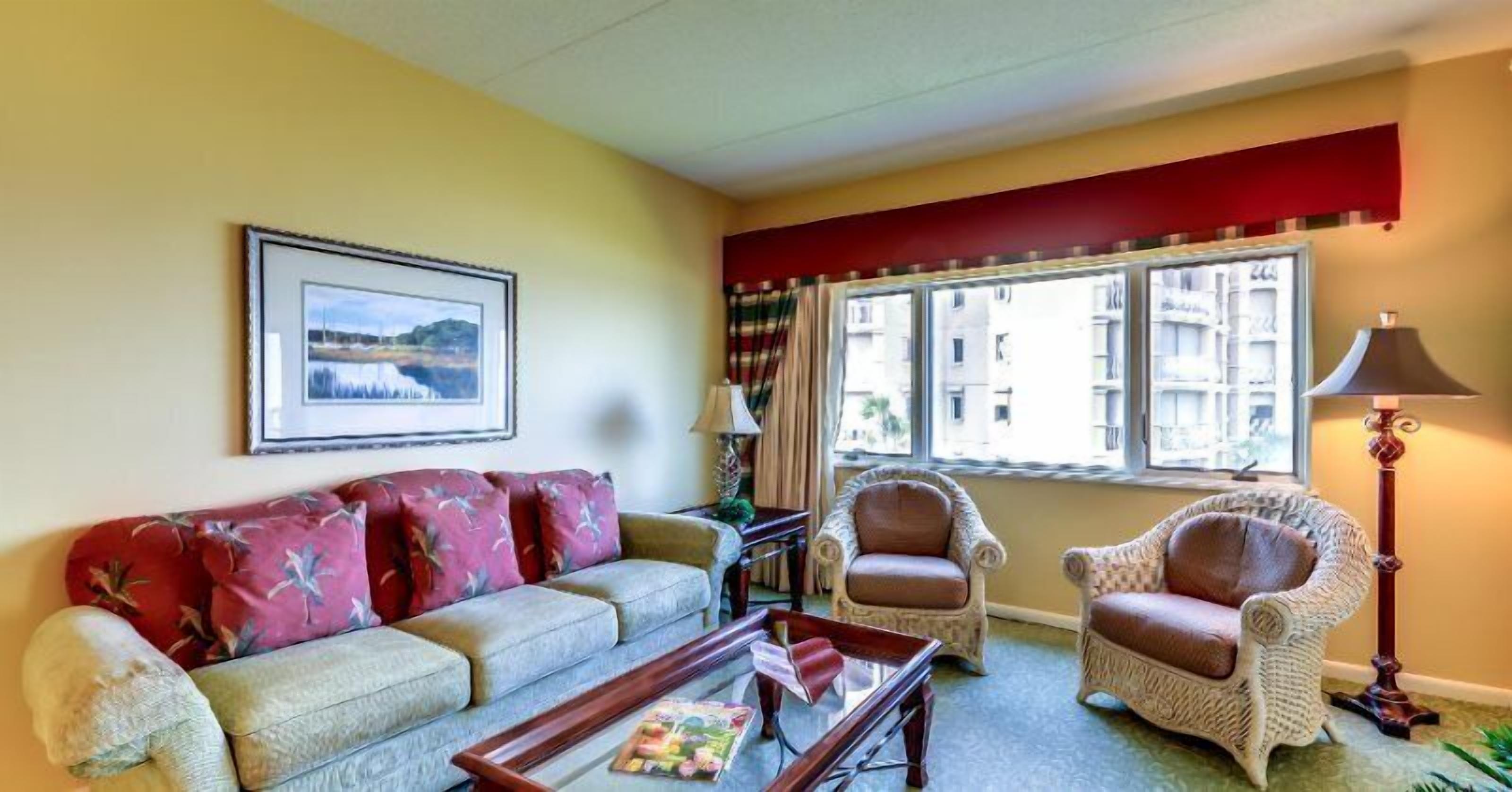 A living room with a sofa, two armchairs, a coffee table, a lamp, and a window with curtains.