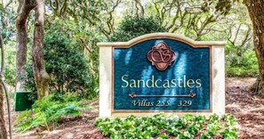 A sign for Sandcastles Villas 255-329 in a wooded area.