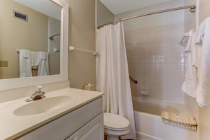 A bathroom with a sink, mirror, toilet, and shower area.