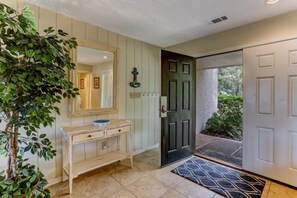 A modern entryway with a white console table, a large mirror, a black door, and a potted plant.