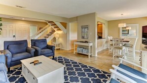 A living room with a staircase, a dining area with white furniture, and a kitchen in the background. - 2100-beachwood (Fernandina Beach)