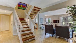 A spacious living area with a wooden staircase, a dining table with chairs, and a view of the outdoors. - 2100-beachwood (Fernandina Beach)