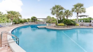 A swimming pool with a curved design, surrounded by palm trees and lounge chairs. - 1129 Beach Walker (Fernandina Beach)