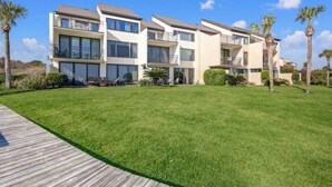 A modern multi-story building with balconies, a well-maintained lawn, and palm trees. - 1129 Beach Walker (Fernandina Beach)