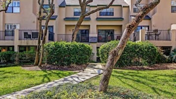 Um edifício residencial com vários andares, varandas, um caminho pavimentado e paisagismo bem cuidado.