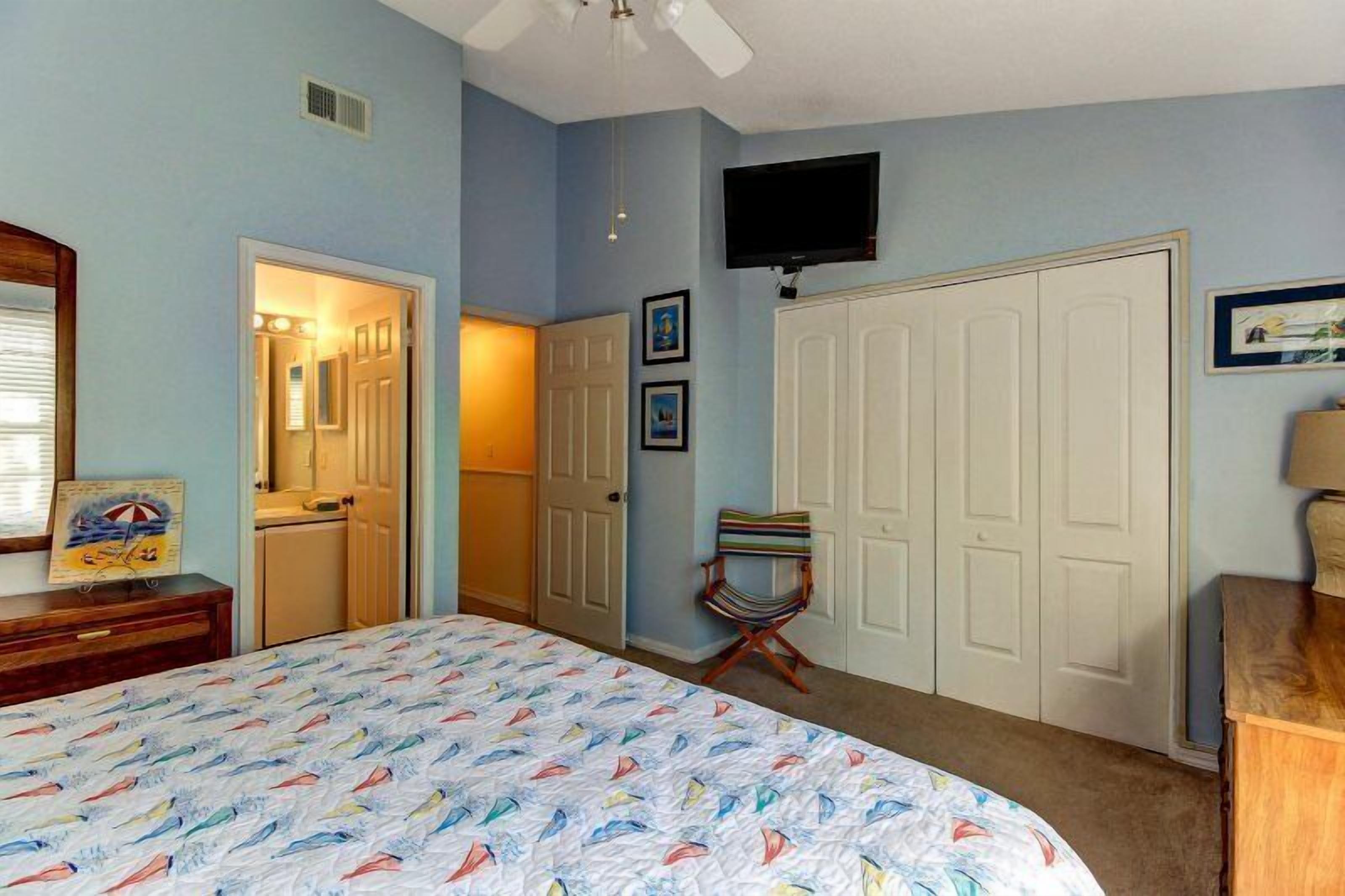A bedroom with a bed, a television mounted on the wall, a door, and a chair.