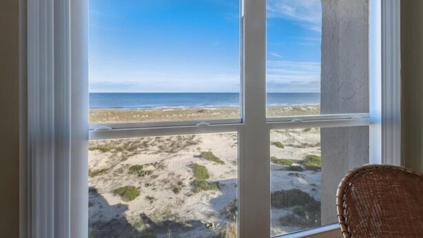 Ett rum med utsikt över en strand genom stora fönster.