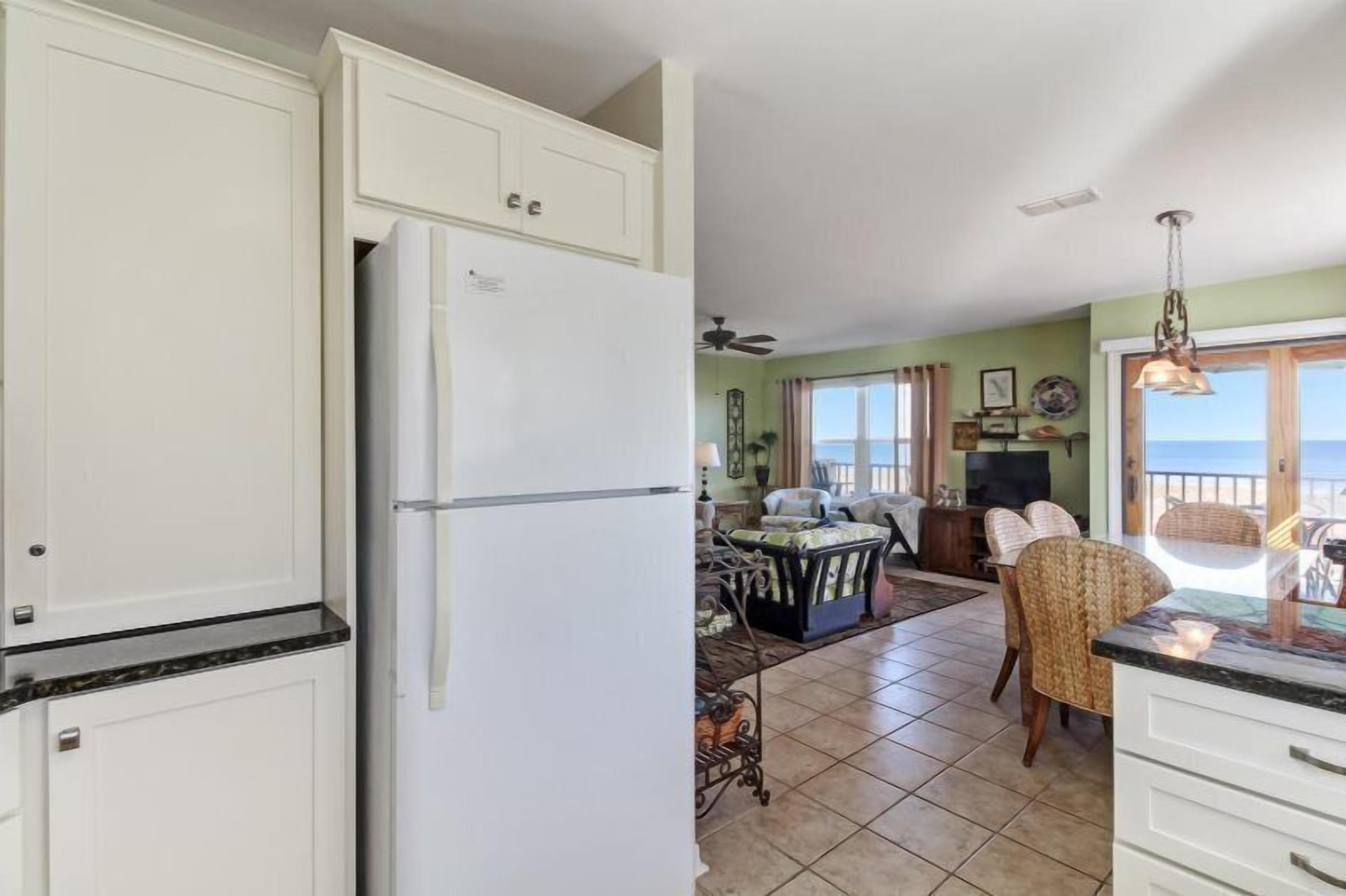 Una cocina con armarios blancos, un refrigerador y un comedor con mesa y sillas.